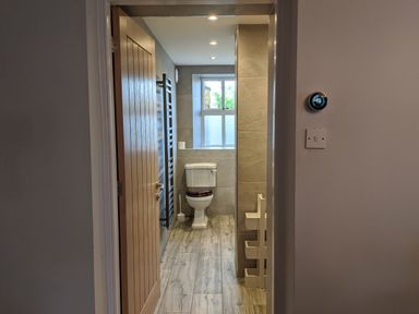 A bathroom with a toilet a wooden door a wall-mounted towel rack and a window at Rose Cottage Lowick Bridge