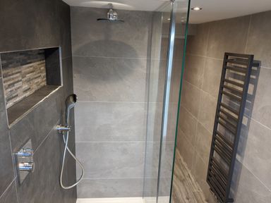 A bathroom with a walk in shower a built in shower shelf and a black towel radiator at Rose Cottage in Lowick Bridge