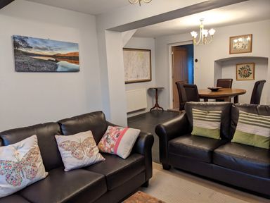 A living room with two black leather sofas and a dining area with round table and four chairs at Rose Cottage in Lowick Bridge