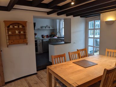 A dining area with a wooden table and chairs next to a kitchen with cabinets and appliances at Rose Cottage in Lowick Bridge