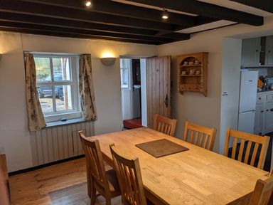 A dining room with a wooden table and chairs near a window and a wooden door at Rose Cottage in Lowick Bridge