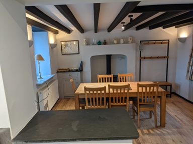 A dining room with a wooden table and six chairs a lamp on a windowsill a cabinet with decorative items and a coat rack at Rose Cottage in Lowick Bridge