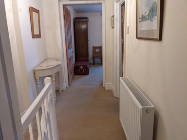 A hallway with a radiator on the right and a white table with a mirror on the left at Rose Cottage in Lowick Bridge
