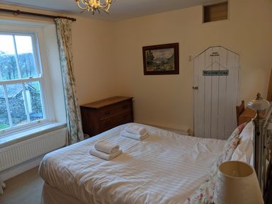 A bedroom with a bed, dresser, window with curtains, and a washroom door at Rose Cottage in Lowick Bridge