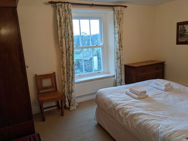 A bedroom with a bed with folded towels a wooden chair a chest of drawers and a window with curtains at Rose Cottage in Lowick Bridge