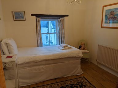 A small bedroom with a single bed a window a chair with a teddy bear a rug and framed pictures on the walls at Rose Cottage in Lowick Bridge