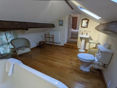 A bathroom with a bathtub chair toilet sink mirror and wooden floor at Rose Cottage in Lowick Bridge