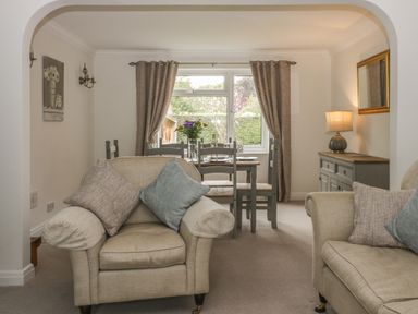 A living room with beige armchairs and a dining table with chairs by a window with curtains at Humble Bee Cottage in Wold Newton near Hunmanby