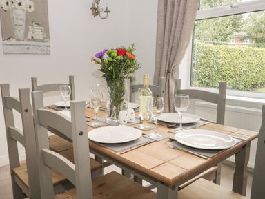 A dining table set with plates wine glasses cutlery flowers and a bottle of wine by a window at Humble Bee Cottage in Wold Newton near Hunmanby