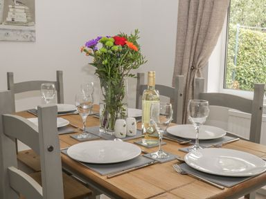 A dining table set with white plates wine glasses a bottle of white wine salt and pepper shakers and a vase of flowers at Humble Bee Cottage in Wold Newton near Hunmanby