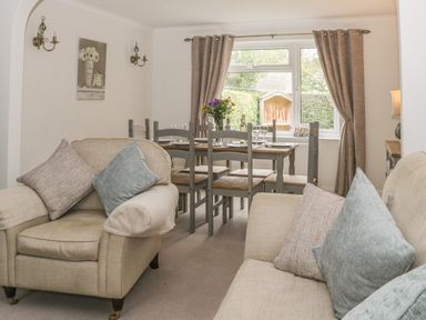 A living room with beige armchairs and a dining table set with chairs near a window with curtains at Humble Bee Cottage in Wold Newton near Hunmanby