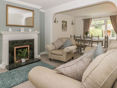 A living room with beige sofas a fireplace with a mirror above and a dining table by a window at Humble Bee Cottage in Wold Newton near Hunmanby