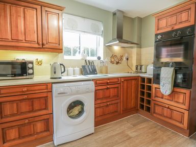 A kitchen with wooden cabinets a microwave kettle washing machine oven and a toaster at Humble Bee Cottage Wold Newton near Hunmanby