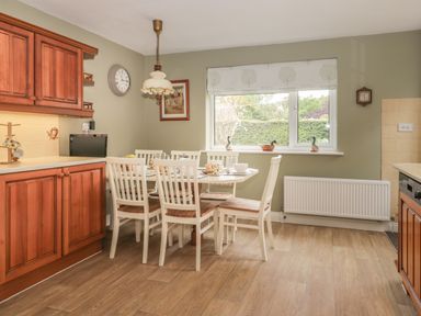A kitchen with wooden cabinets white dining table and chairs and a window with decorative ducks at Humble Bee Cottage in Wold Newton near Hunmanby
