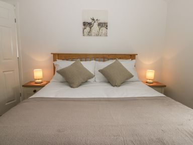 A bedroom with a wooden bed frame white bedding two beige pillows two bedside tables with lamps and a deer painting on the wall at Humble Bee Cottage in Wold Newton near Hunmanby