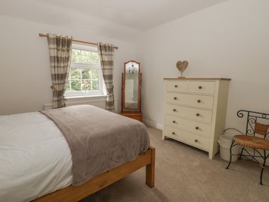A bedroom with a wooden bed a chest of drawers a standing mirror and a window with curtains at Humble Bee Cottage in Wold Newton near Hunmanby