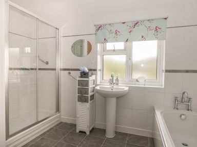 A bathroom with a shower, pedestal sink, storage unit, and bathtub at Humble Bee Cottage in Wold Newton near Hunmanby