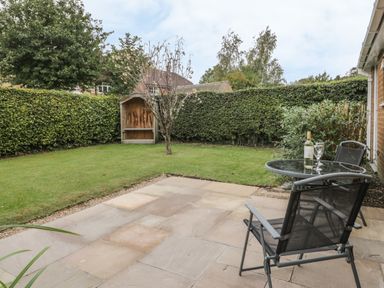 A patio with a round glass table and two chairs overlooking a lawn with a tree and a wooden bench at Humble Bee Cottage in Wold Newton near Hunmanby