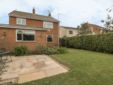 A backyard with a patio area, grass lawn, plants, and a brick house at Humble Bee Cottage in Wold Newton near Hunmanby