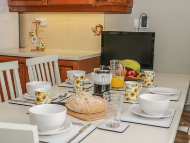 A kitchen table set with white bowls and sunflower print mugs with bread orange juice and fruit at Humble Bee Cottage in Wold Newton near Hunmanby
