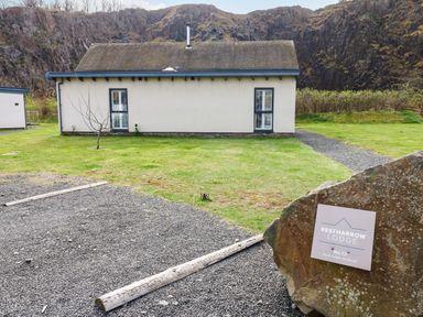 A small lodge with two windows and a grassy yard surrounded by rocky hills at Restharrow Lodge Bamburgh