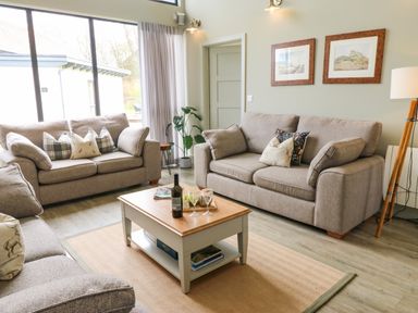 A living room with three sofas a coffee table and framed pictures on the wall at Restharrow Lodge in Bamburgh