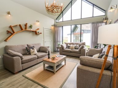 A living room with three sofas a wooden coffee table and large windows at Restharrow Lodge in Bamburgh