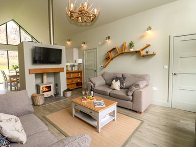 A living room with beige sofas a wooden coffee table a wall-mounted TV and a wood-burning stove at Restharrow Lodge in Bamburgh