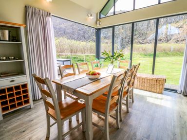 A dining area with a wooden table and chairs by large windows overlooking a garden at Restharrow Lodge in Bamburgh