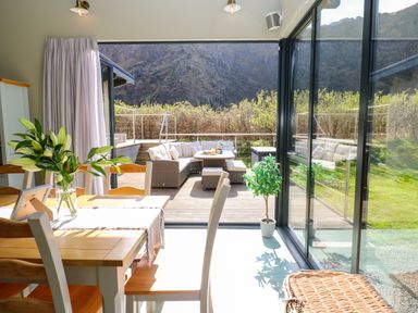 A dining area with wooden table and chairs and glass doors opening to an outdoor patio with seating and cushions at Restharrow Lodge in Bamburgh