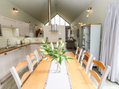 A kitchen and dining area with a wooden table and chairs and white cabinets at Restharrow Lodge in Bamburgh