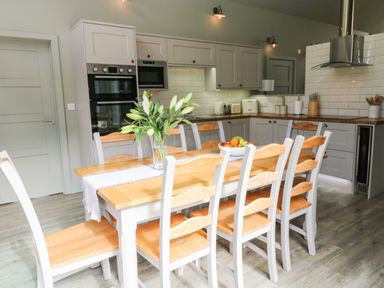 A kitchen with wooden dining table and chairs a vase with flowers and fruit bowl on the table at Restharrow Lodge in Bamburgh