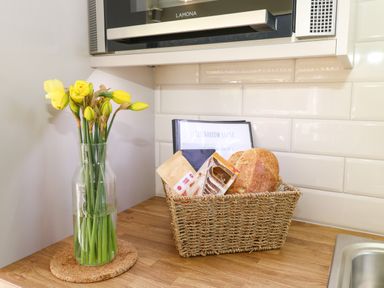 A kitchen countertop with a vase of yellow flowers a wicker basket containing bread and packaged goods under a microwave at Restharrow Lodge in Bamburgh