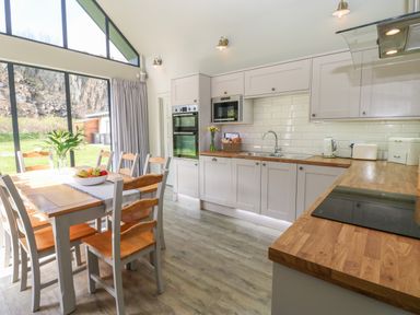 A kitchen with wooden countertops dining table with chairs and large windows showing outdoor landscape at Restharrow Lodge in Bamburgh