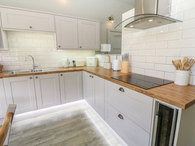 A kitchen with white cabinets wooden countertops a sink an electric stove and kitchen utensils at Restharrow Lodge in Bamburgh