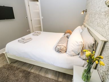 A bedroom with a bed with pillows and folded towels a vase with flowers on a bedside table and a wall mounted television at Restharrow Lodge in Bamburgh
