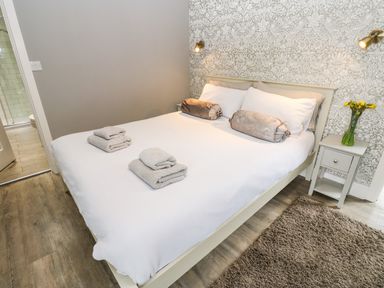 A bedroom with a white bedspread two bedside tables and a door leading to a bathroom at Restharrow Lodge in Bamburgh