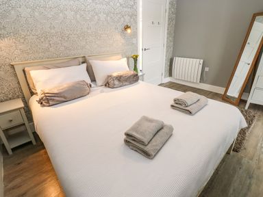 A bedroom with a bed and folded towels on it a chair a standing mirror and bedside tables at Restharrow Lodge in Bamburgh