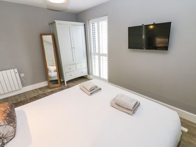 A bedroom with a bed and towels on it a wardrobe a standing mirror and a wall mounted TV at Restharrow Lodge in Bamburgh