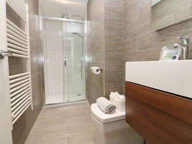 A bathroom with a shower enclosure toilet with towels and toilet paper and a sink with wooden cabinet at Restharrow Lodge in Bamburgh