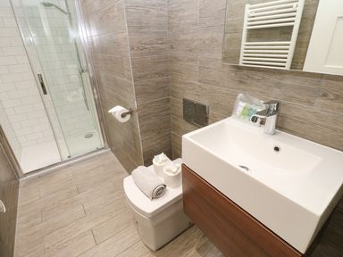 A bathroom with a shower cabin a toilet with towels and toilet paper and a sink with toiletries at Restharrow Lodge in Bamburgh