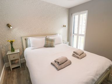 A bedroom with a large bed with folded towels on top bedside tables with lamps and a vase of yellow flowers at Restharrow Lodge in Bamburgh