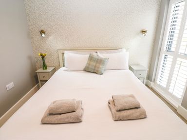 A bedroom with a bed with white bedding two bedside tables with lamps and a vase with flowers at Restharrow Lodge in Bamburgh