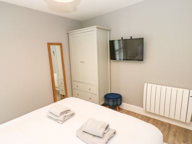 A bedroom with a bed and towels a standing mirror a white wardrobe a wall-mounted television and a small stool at Restharrow Lodge in Bamburgh