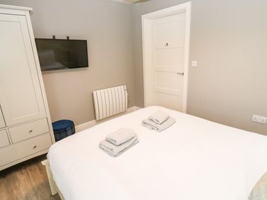A bedroom with a bed with folded towels a wall mounted TV a white wardrobe and a closed door at Restharrow Lodge in Bamburgh