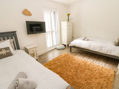 A bedroom with two single beds a wall mounted tv a chest of drawers a bedside table and a rug at Restharrow Lodge in Bamburgh