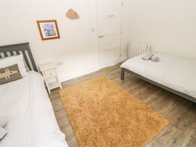 A bedroom with two single beds separated by a small white nightstand and a tan rug on wooden floor at Restharrow Lodge in Bamburgh