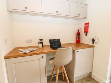 A small workspace with a wooden countertop laptop cup fire extinguisher and a chair at Restharrow Lodge in Bamburgh