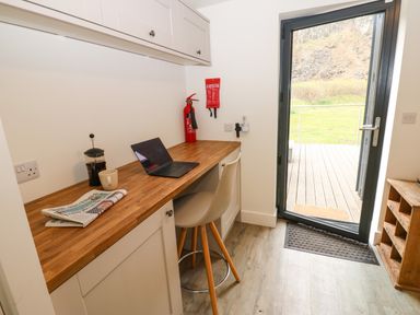 A small workspace with a wooden countertop chair laptop coffee press and newspaper next to a glass door at Restharrow Lodge in Bamburgh