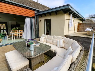 An outdoor seating area with a glass table and cushioned wicker sofas next to an open dining room at Restharrow Lodge in Bamburgh